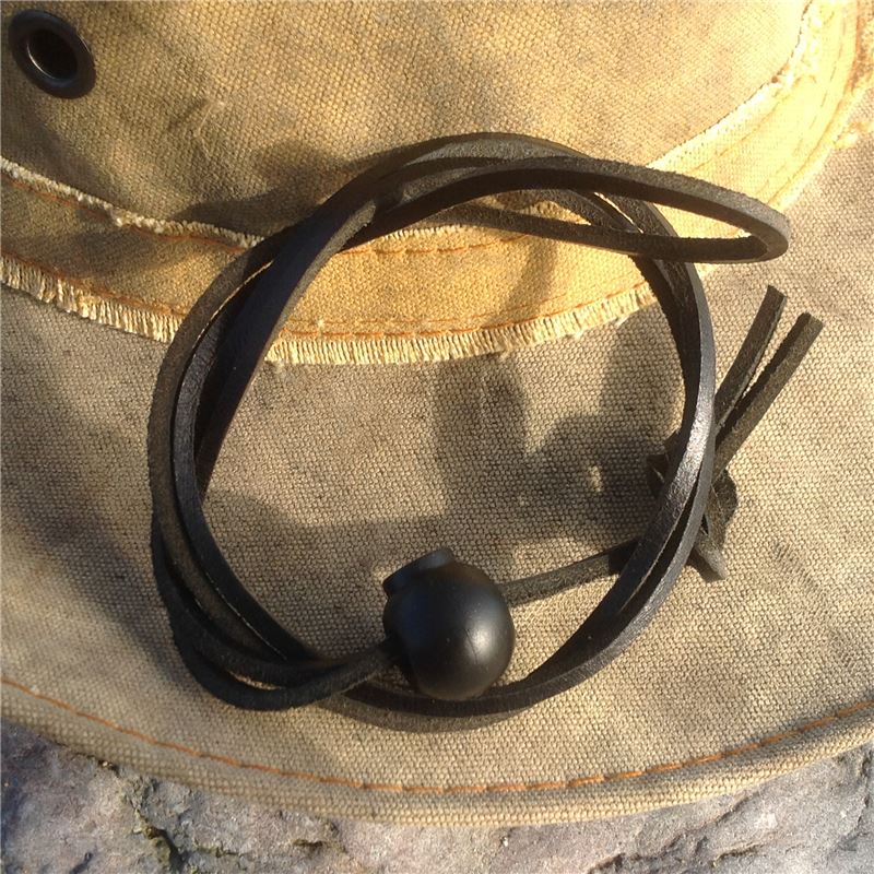 A black leather bracelet with a round black bead, resting on a beige canvas hat.